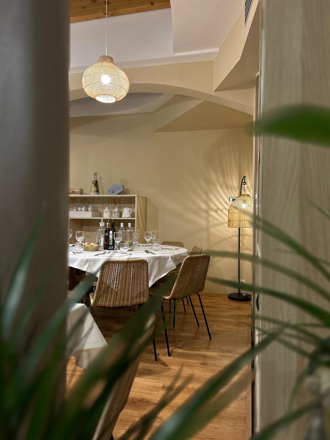 La sala di Livello: tavolo rotondo apparecchiato con tovaglia bianca, sedie in rattan e lampade in vimini dalla luce calda